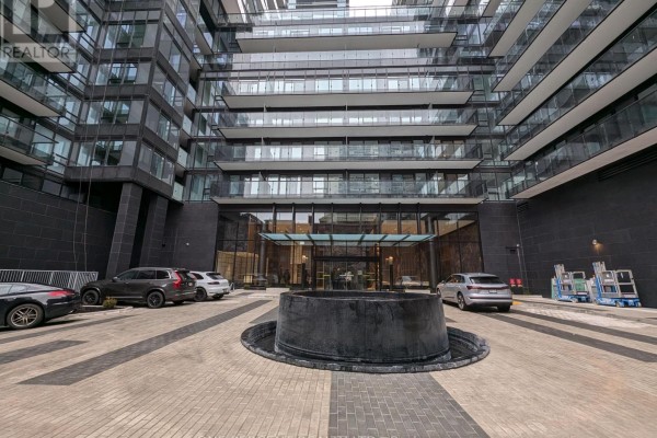 Entrance courtyard with a water feature, surrounded by parked cars and modern buildings. - 1104 - 127 Broadway Avenue, Toronto