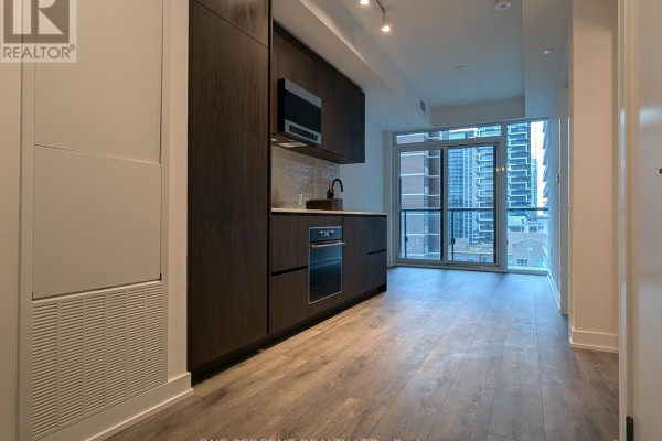 Kitchen area featuring dark cabinetry, stainless steel appliances, and a large window with city views. - 1104 - 127 Broadway Avenue, Toronto