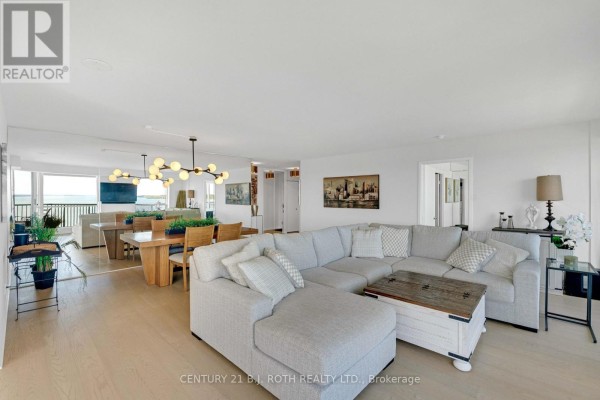 Open concept living and dining area with a large sectional sofa and expansive windows. - 1104 - 65 Ellen Street, Barrie