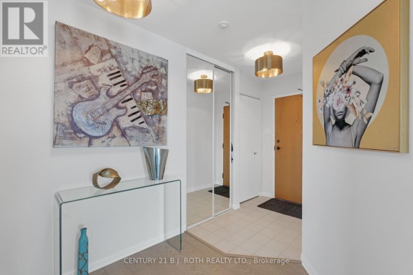 Apartment hallway with a glass console table, mirrored closet doors, and abstract wall art. - 1104 - 65 Ellen Street, Barrie