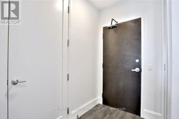 Interior hallway with a dark wood apartment door, white walls, and silver door handles. - 1105 - 112 King Street E, Hamilton