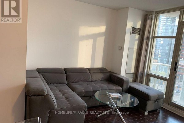 Living room showing a large grey sectional sofa and a glass coffee table. - 1105 - 35 Mariner Terrace, Toronto