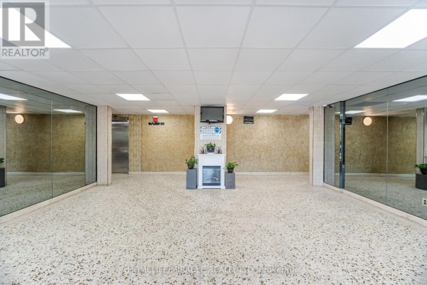 Lobby with beige speckled floor, mirrored walls, elevator, and a decorative fireplace. - 1105 - 60 Stevenson Road, Toronto