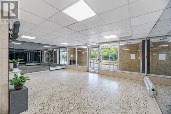 View of apartment building lobby with glass doors leading outside, mirrored walls, and plants. - 1105 - 60 Stevenson Road, Toronto