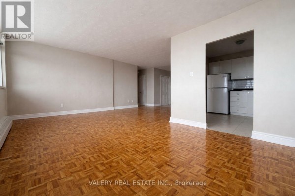 Empty living area with parquet floors and an opening to the kitchen. - 1105 - 890 Jane Street, Toronto