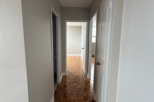 Hallway with parquet flooring, leading to a bathroom and bedroom doors. - 1105 - 890 Jane Street, Toronto