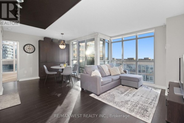 Open concept living and dining area with grey sectional sofa and large windows. - 1106 - 15 Iceboat Terrace, Toronto