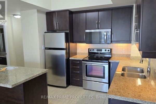 Kitchen with dark wood cabinets, stainless steel appliances, granite counters, and island. - 1106 - 50 Absolute Avenue, Mississauga