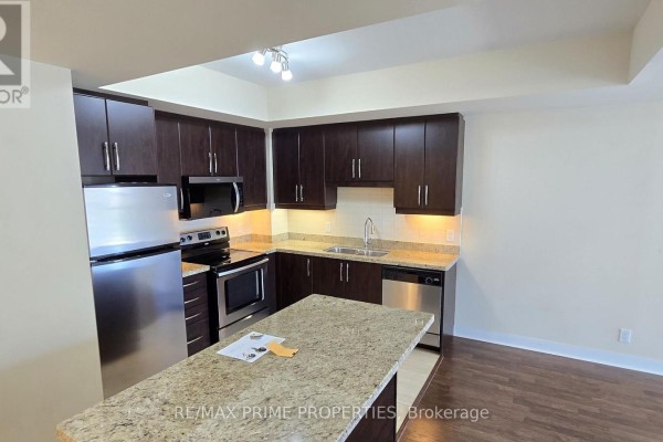 Open-concept kitchen with dark cabinets, stainless steel appliances, granite island, and dark wood floor. - 1106 - 50 Absolute Avenue, Mississauga