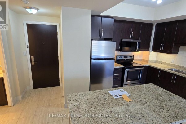 View of a modern kitchen with dark cabinets and a granite island, opening to a hallway. - 1106 - 50 Absolute Avenue, Mississauga