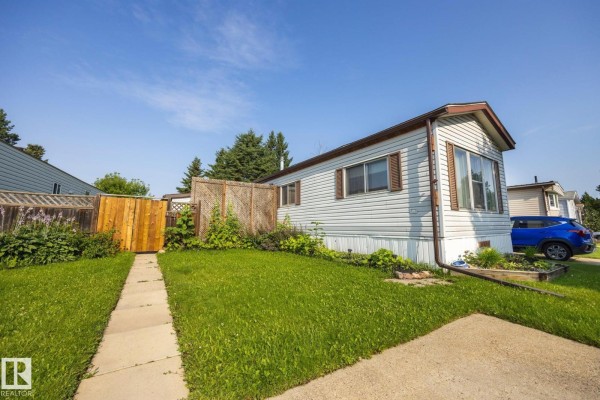 Exterior of a mobile home with white siding, green grass, and a paved walkway. - 1106 Lake Vista Dr, Sherwood Park