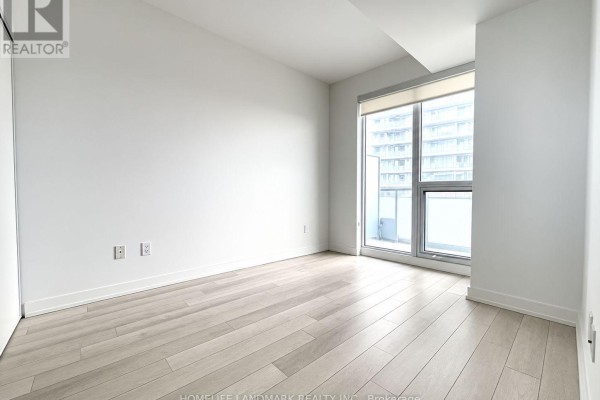 Bright bedroom with white walls, light wood floors, and a large window with city view. - 1107 - 115 Mcmahon Drive, Toronto