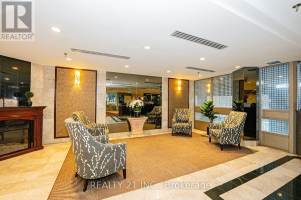 Lobby seating area with upholstered chairs, a fireplace, and mirrored walls. - 1107 - 3233 Eglinton Avenue E, Toronto