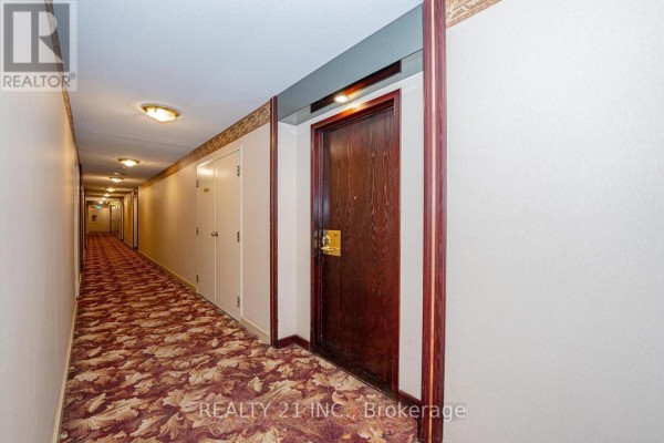 Long, carpeted apartment building hallway with wood doors and overhead lighting. - 1107 - 3233 Eglinton Avenue E, Toronto