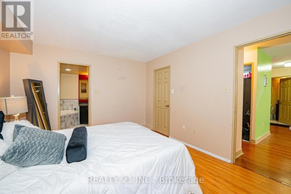 Bedroom with a large bed, light pink walls, wooden floors, and closet doors. - 1107 - 3233 Eglinton Avenue E, Toronto