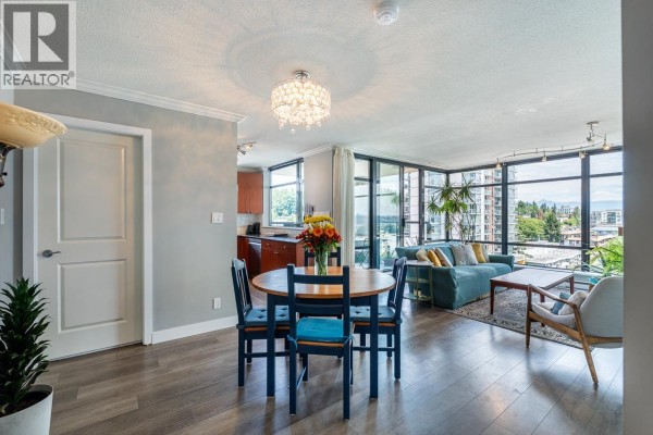 Apartment dining area with wooden table, blue chairs, and living room beyond. - 1107 610 Victoria Street, New Westminster
