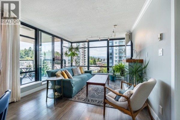 Apartment living room with teal sofa, armchair, coffee table, and large windows. - 1107 610 Victoria Street, New Westminster
