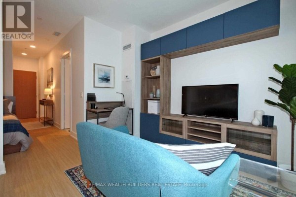 Living area with teal sofa, built-in entertainment unit, and view of hallway and bedroom. - 1108 - 7 Grenville Street, Toronto