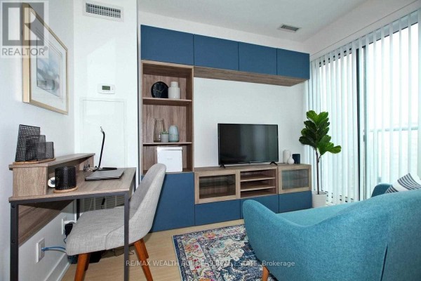 Desk and chair in living area with built-in entertainment unit and sliding glass door. - 1108 - 7 Grenville Street, Toronto
