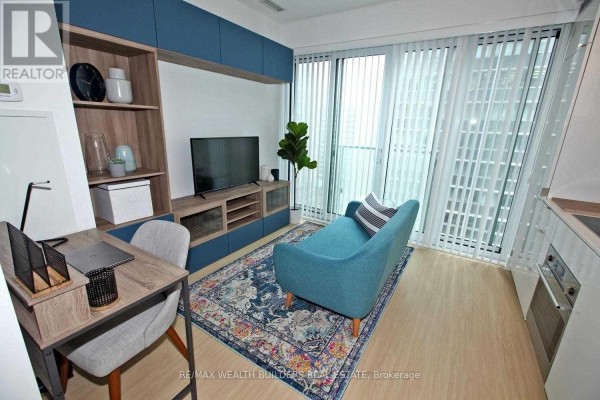 Living room with teal sofa, desk, entertainment unit, and floor-to-ceiling window with vertical blinds. - 1108 - 7 Grenville Street, Toronto