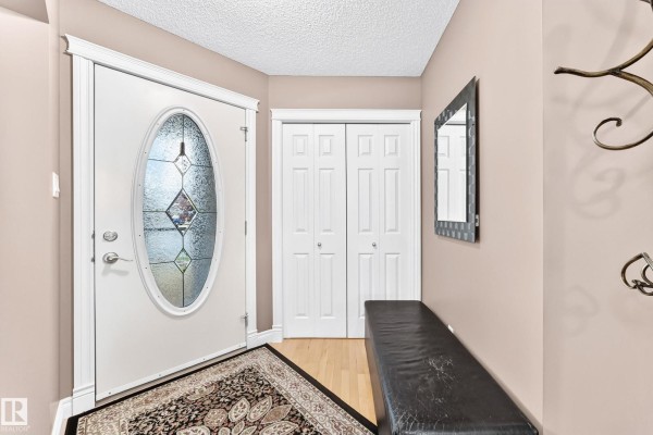 Entryway with a white oval glass front door, beige walls, and a black leather bench. - 1108 117 St Sw, Edmonton