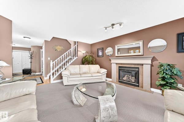 Living room with stairs, a fireplace, beige carpet, and white leather furniture. View towards entryway. - 1108 117 St Sw, Edmonton