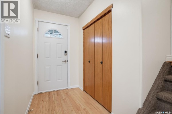 Entranceway with a white door, wood closet doors, and wood laminate flooring. - 1108 Tiffin Crescent, Saskatoon