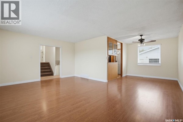 Living room with wood laminate flooring, cream walls, and a view of the stairs. - 1108 Tiffin Crescent, Saskatoon