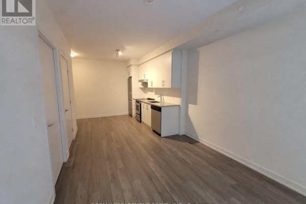 View of the living area showcasing light wood flooring and kitchen appliances against a neutral wall. - 1109 - 212 King William Street, Hamilton