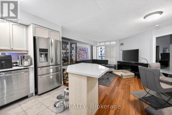 A kitchen with stainless steel appliances and an island, open to the living area. - 1109 - 5 Northtown Way, Toronto