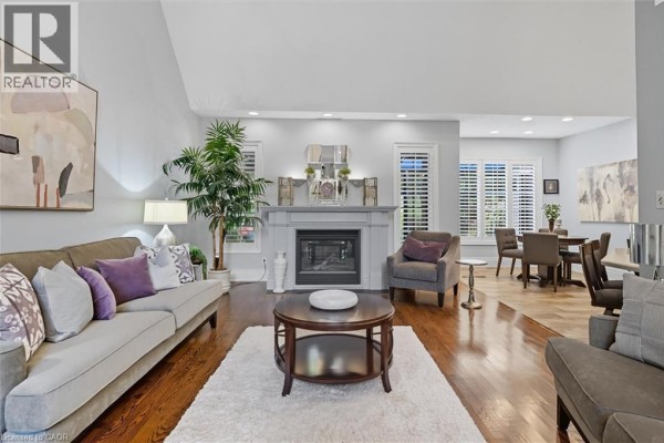 Living room with a grey fireplace, sofa, armchair, coffee table, and dining area beyond. - 1109 Forestvale Drive, Burlington