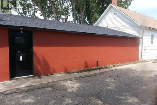 Side view of the red stucco building with a black door and asphalt exterior. - 1109 South Railway Street E, Swift Current