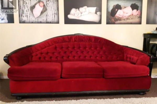Close-up of a red velvet tufted sofa with a dark wood frame. - 1109 South Railway Street E, Swift Current