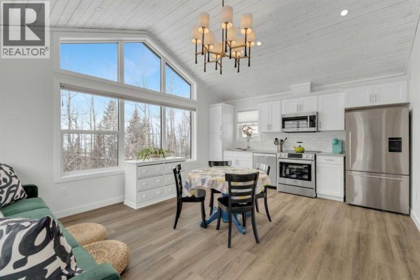 Living and dining area with a green sofa, wood-look flooring, and white wood-paneled ceiling. - 111, 41310 Range Road 282, Rural Lacombe County