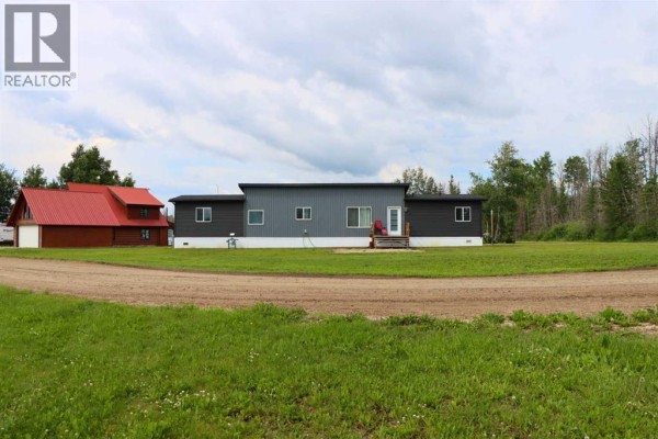 Front exterior of the mobile home with dark grey and grey siding, surrounded by a grassy field and trees. - 111, 71127 Range Road 234, Rural Greenview No  16, M D  Of