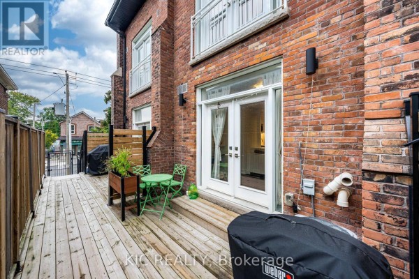 Wooden deck with green patio furniture and a barbecue against a red brick building exterior. - 111 - 1183 Dufferin Street, Toronto