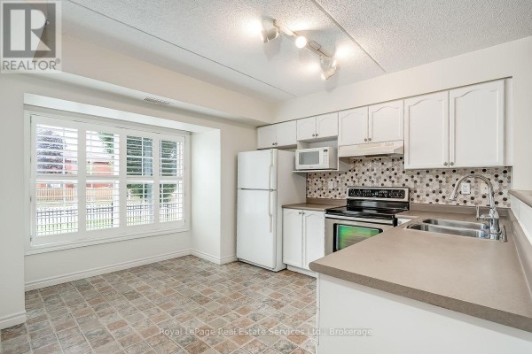 Kitchen with white cabinets, stainless steel appliances, and tiled floor. - 111 - 1460 Bishops Gate, Oakville