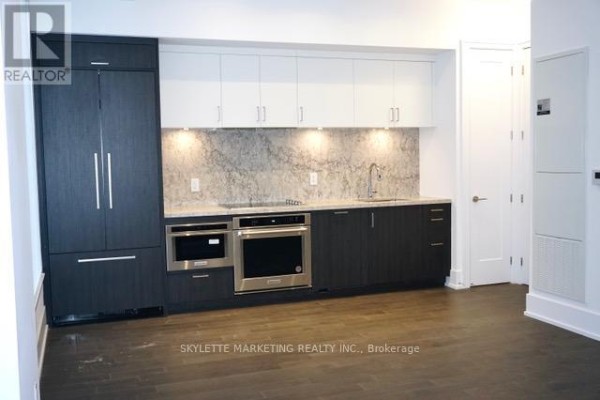 Kitchen area with dark lower cabinets, white upper cabinets, and integrated appliances. - 111 - 25 Adra Grado Way, Toronto