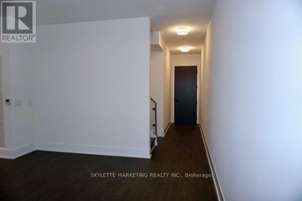 Interior hallway with dark wood floors, white walls, and a dark front door. - 111 - 25 Adra Grado Way, Toronto