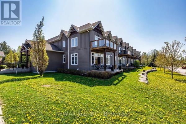 Rear view of a townhouse complex with wooden balconies and surrounding green lawn. - 111 - 29 Lakewood Crescent, Kawartha Lakes