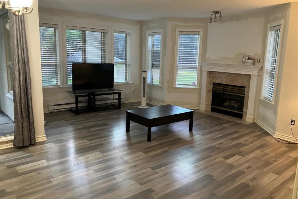 Living room with fireplace, television, coffee table, and large windows - 111 2575 Ware Street, Abbotsford