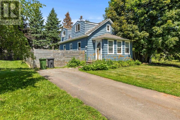Side view of the blue house with a driveway and surrounding greenery. - 111 Beach Grove, Charlottetown