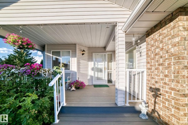 Close-up of the covered front porch with white railings, pendant lights, and hanging flower baskets. - 111 Lakeside Pl, Leduc