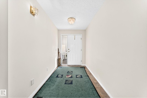 Interior entryway with light beige walls, a green floral rug, and a white front door with sidelight. - 111 Lakeside Pl, Leduc
