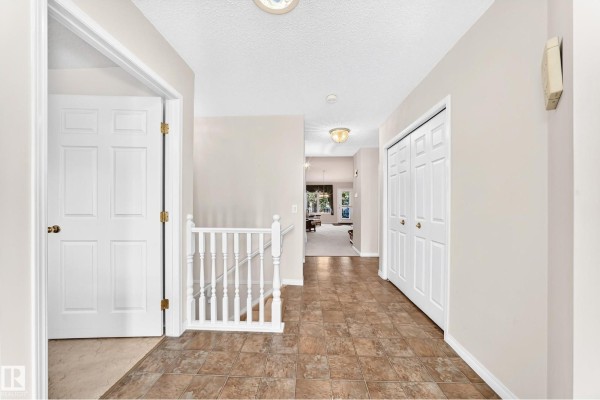 Hallway inside the duplex showing tiled flooring, a white staircase railing, and bi-fold closet doors. - 111 Lakeside Pl, Leduc