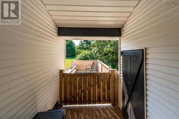 View through a covered carport to a wooden deck with chairs and trees beyond. - 111 Prince William Street, Digby