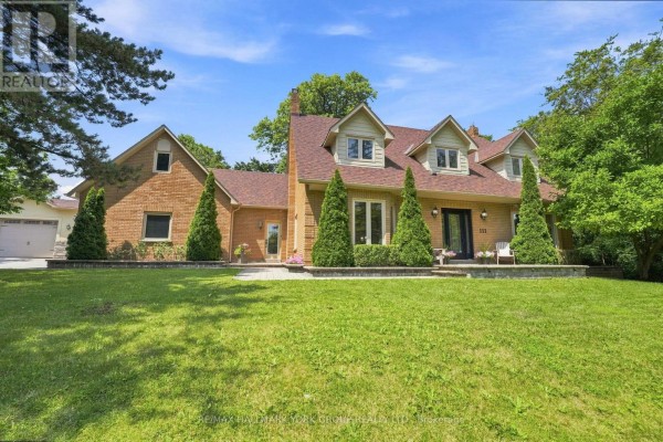 Front exterior of a residential brick house with a large green lawn, manicured bushes, and a paved walkway. - 111 Whispering Pine Trail, Aurora