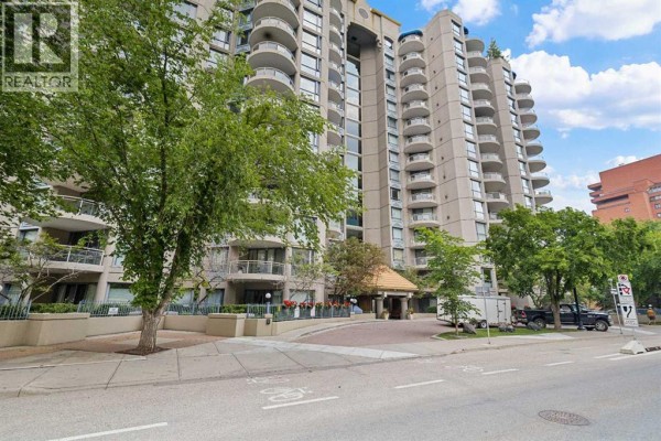 Street view of the apartment building entrance with trees and parked vehicles. - 1110, 804 3 Avenue Sw, Calgary