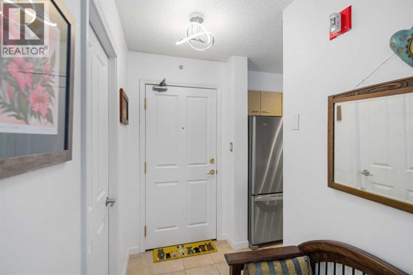 Apartment entryway with white doors, stainless steel refrigerator, and mirror. - 1110, 804 3 Avenue Sw, Calgary