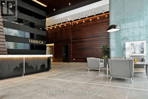 Modern apartment building lobby with wood paneling, reception desk, and grey seating. - 1110 - 179 Metcalfe Street, Ottawa